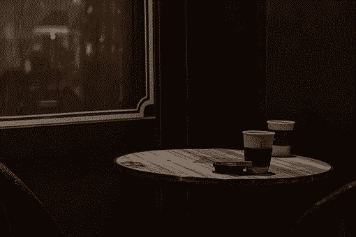 Two coffee cups sitting on a wooden table infornt of the window