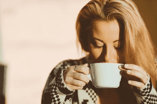 A blonde woman sipping on a white cup of coffee
