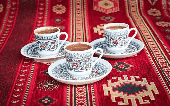 Three cups with blue and white designs filled with turkish coffee on top of saucers and placed on top of a red carpet