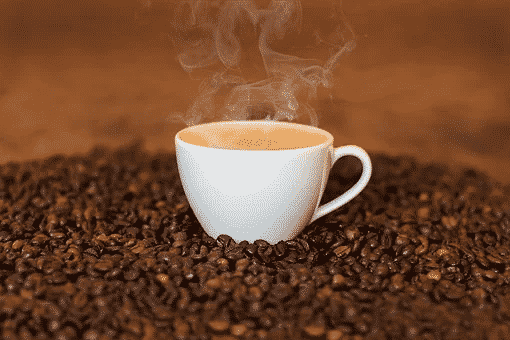 a white mug of steaming coffee placed on top of a lot of coffee beans