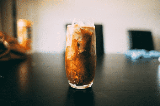 A glass of cold blakc coffee with milk swirling in it with ice cubes