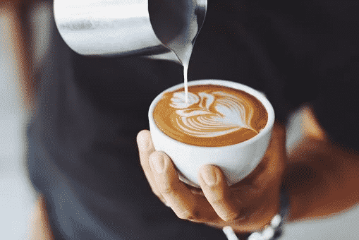 A man holding a white cup of coffee and dripping milk in it to make coffee art