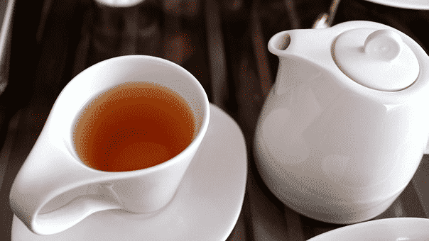 A white cup full of green coffee sitting besides a white kettle